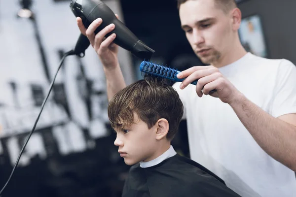 Le coiffeur fait une jolie coiffure à la mode pour le garçon dans un salon de coiffure moderne . — Photo