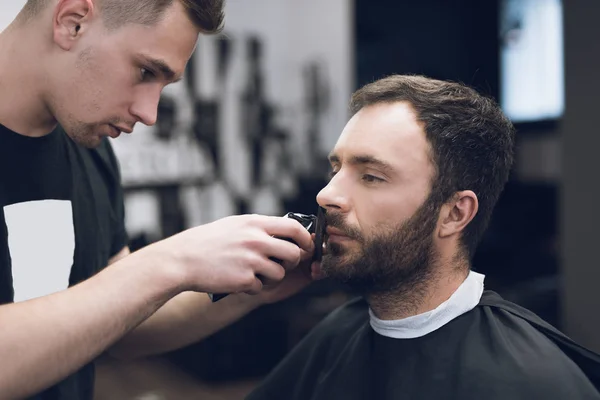 Barbier coupe une barbe à un homme dans un salon de coiffure . — Photo