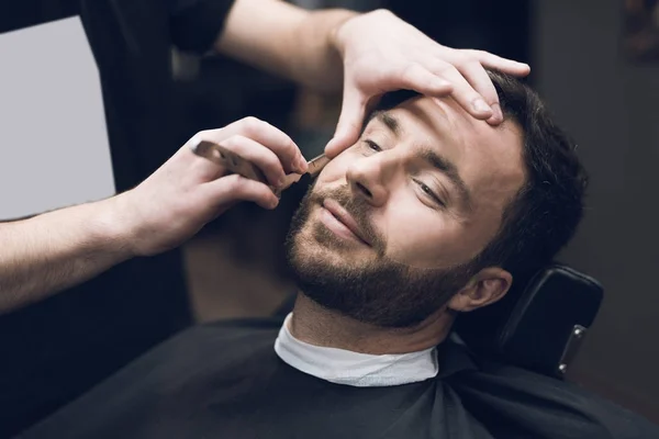 Fryzjer goli jego głowy, wąsy i brodę do człowieka w salonie fryzjerskim. — Zdjęcie stockowe