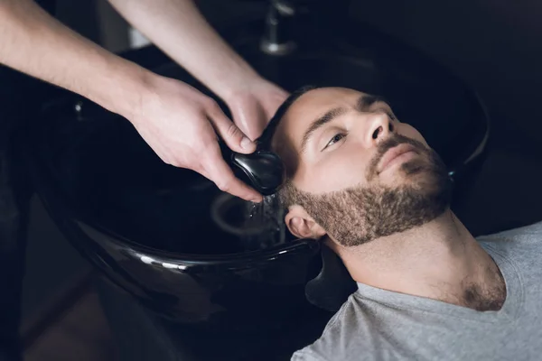 Il parrucchiere lava la testa della doccia nel lavandino del barbiere . — Foto Stock