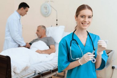 Yaşlı adam yalanlar üzerine bir karyola tıbbi koğuşta ve onun yanında var olan bir doktor ve bir hemşire.