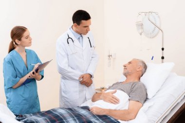 Yaşlı adam tıbbi koğuşta yatak üzerinde yatıyor. Onun yanında bir doktor ve bir hemşire olduğunu.
