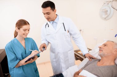 Yaşlı adam tıbbi koğuşta yatak üzerinde yatıyor. Onun yanında bir doktor ve bir hemşire olduğunu.
