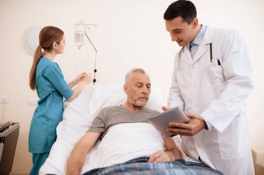 Yaşlı adam yalanlar üzerine bir karyola tıbbi koğuşta ve onun yanında bir doktor duruyor. O tablet yaşlı adam için bir şeyler gösteriyor