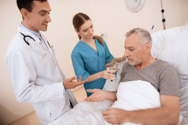 Yaşlı adam yalanlar üzerine bir karyola tıbbi koğuşta ve onun yanında var olan bir doktor ve bir hemşire.