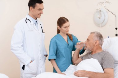 Yaşlı adam yalanlar üzerine bir karyola tıbbi koğuşta ve onun yanında var olan bir doktor ve bir hemşire.