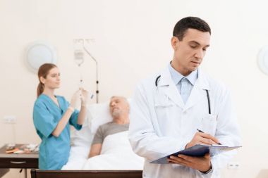 Yaşlı adam yalanlar üzerine bir karyola tıbbi koğuşta ve onun yanında var olan bir doktor ve bir hemşire.