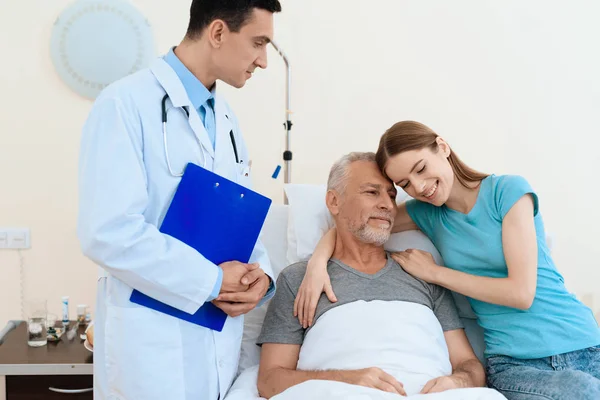 Um homem idoso jaz em um quarto de hospital em uma cama. Está em reabilitação. Ao lado dele está um médico. . — Fotografia de Stock