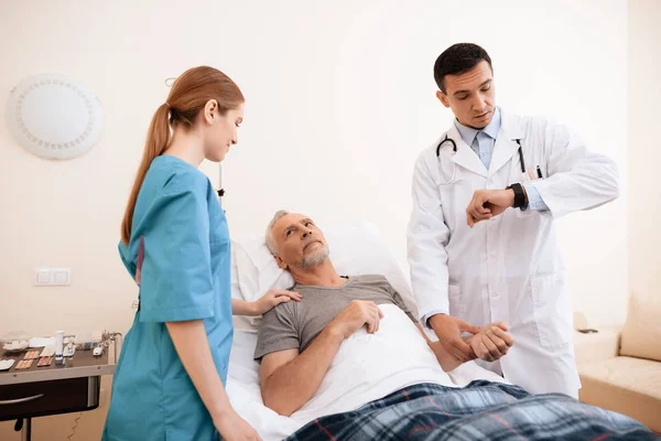 Starý muž leží na lehátku v lůžkového oddělení. Vedle něj je lékař a zdravotní sestra. — Stock fotografie