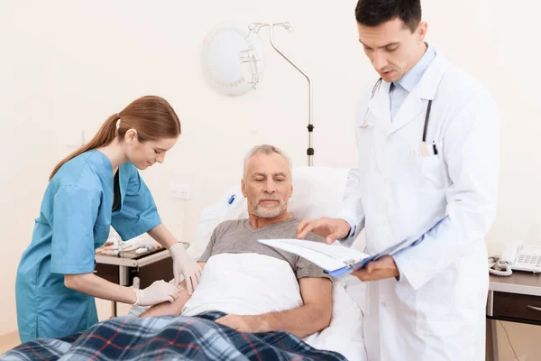 Der alte Mann liegt auf einem Feldbett in der Krankenstation, neben ihm ein Arzt und eine Krankenschwester. — Stockfoto