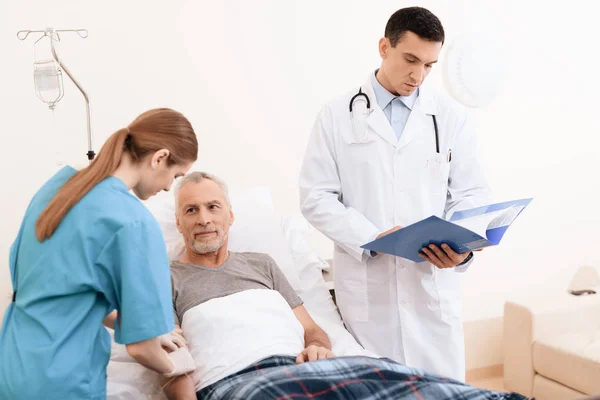 Starý muž leží na lehátku na lékařské oddělení a hned po něm tam je lékař a zdravotní sestra. — Stock fotografie