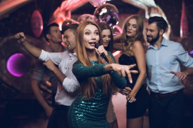 Yeşil giysili bir kadına bir karaoke kulüpte arkadaşlarıyla şarkıları söyleyerek var. Arkadaşlarıyla eğlenmek arka plan üzerinde.