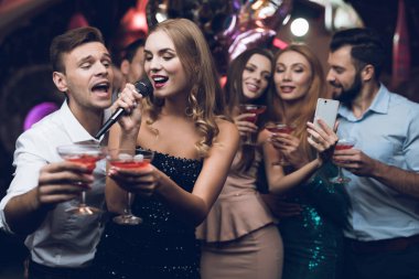 Siyah elbiseli bir kadın bir karaoke kulüpte arkadaşlarıyla şarkıları söyleyerek var. Arkadaşları selfie yapmak.