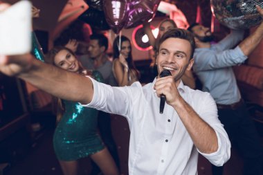 Beyaz gömlekli bir adam bir gece kulübünde şarkı söylüyor. O elinde bir mikrofon var.