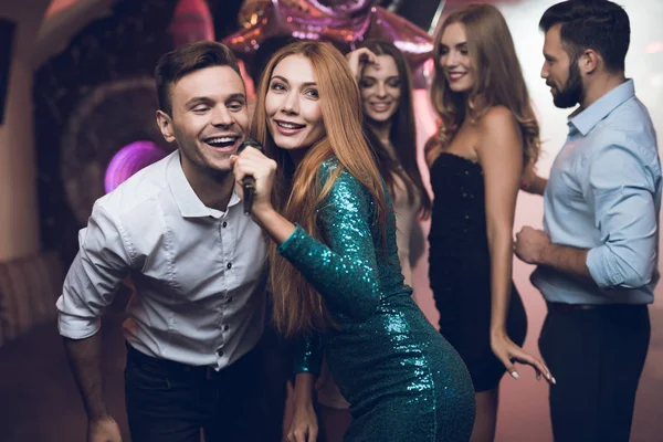 Una mujer con un vestido verde está cantando canciones con sus amigos en un club de karaoke. Sus amigos se divierten en el fondo . — Foto de Stock