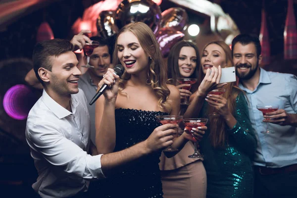 Žena v černých šatech je zpívat písně se svými přáteli v karaoke klubu. Její přátelé dělají selfie. — Stock fotografie