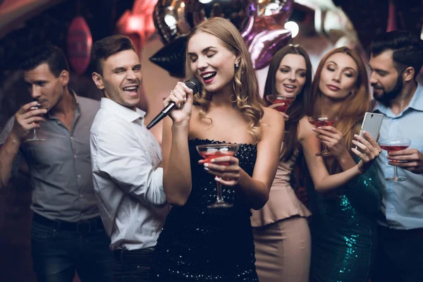 Eine Frau im schwarzen Kleid singt mit ihren Freundinnen in einem Karaoke-Club Lieder. Ihre Freundinnen haben Spaß im Hintergrund. — Stockfoto