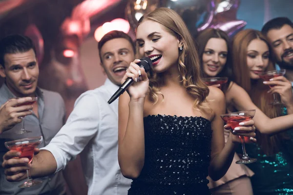 Una mujer vestida de negro está cantando canciones con sus amigos en un club de karaoke. Sus amigos se divierten en el fondo . — Foto de Stock