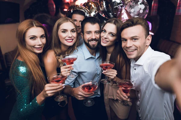 Ein Mann macht Selfie mit seinen Freunden. Er hat Spaß in einem Nachtclub. Im Hintergrund stehen seine Freunde mit Cocktails. — Stockfoto