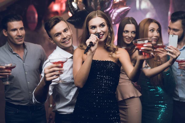 Eine Frau im schwarzen Kleid singt mit ihren Freundinnen in einem Karaoke-Club Lieder. Ihre Freundinnen haben Spaß im Hintergrund. — Stockfoto