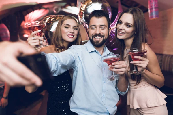 Um homem faz selfie com os amigos. Ele diverte-se numa discoteca. Contra o fundo estão seus amigos com coquetéis . — Fotografia de Stock