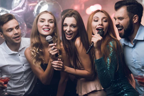 Três raparigas bonitas cantam num clube de karaoke. Atrás deles há homens esperando por sua vez . — Fotografia de Stock