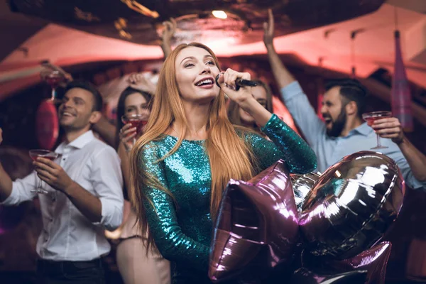 Os jovens se divertem em uma boate e cantam no karaoke. Em primeiro plano, uma mulher de vestido verde . — Fotografia de Stock