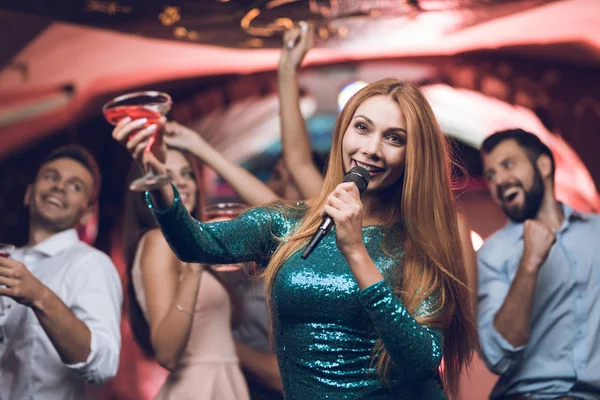 Los jóvenes se divierten en un club nocturno y cantan en el karaoke. En primer plano, una mujer con un vestido verde . — Foto de Stock