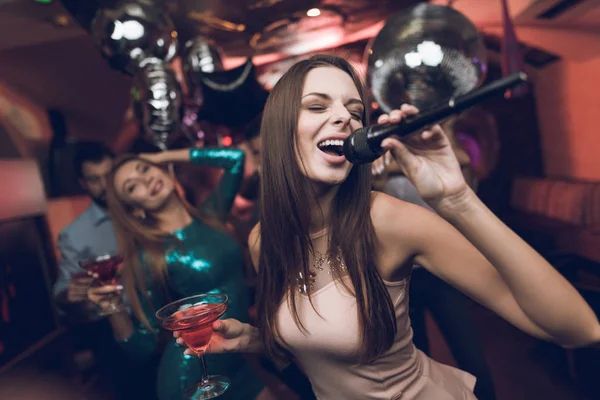 Die jungen Leute amüsieren sich in einem Nachtclub und singen Karaoke. Im Vordergrund eine Frau in einem beigen Kleid. — Stockfoto