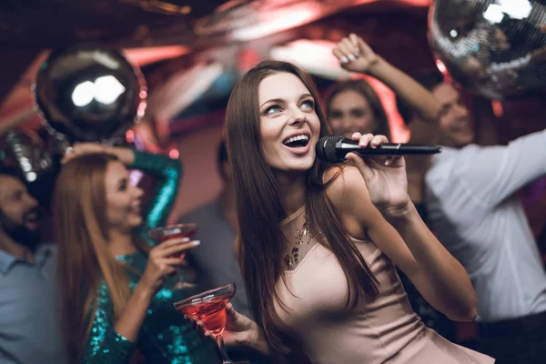 Młodzi ludzie bawić się w klubie nocnym i śpiewać w karaoke. Na pierwszym planie jest kobieta w sukni beżowy. — Zdjęcie stockowe