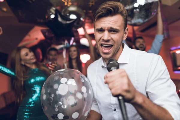 Los jóvenes se divierten en un club nocturno y cantan en el karaoke. En primer plano hay un hombre con una camisa blanca . — Foto de Stock