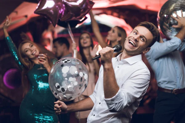 Молодые люди веселятся в ночном клубе и поют в караоке. На переднем плане мужчина в белой рубашке . — стоковое фото