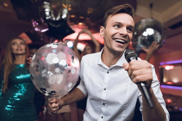 Los jóvenes se divierten en un club nocturno y cantan en el karaoke. En primer plano hay un hombre con una camisa blanca . — Foto de Stock