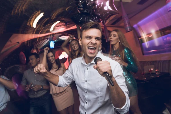 Un hombre con camisa blanca está cantando en un club nocturno. Tiene un micrófono en sus manos. . — Foto de Stock