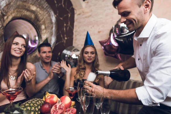 Мужчина открывает шампанское, чтобы выпить с друзьями. Они сидят в клубе за столом и отдыхают после танцев. . — стоковое фото
