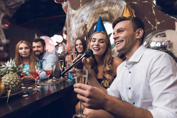 Los jóvenes están descansando en un club nocturno de moda. Un tipo con una camisa blanca y una chica con un vestido negro están cantando . —  Fotos de Stock