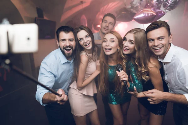 Jóvenes en el club cantan canciones, bailan y hacen selfies en un smartphone con autoadhesivo . — Foto de Stock