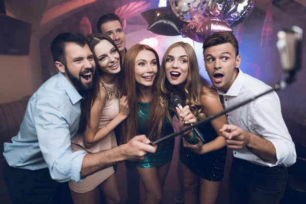 Jóvenes en el club cantan canciones, bailan y hacen selfies en un smartphone con autoadhesivo . — Foto de Stock
