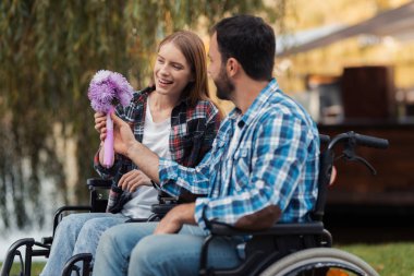 Sakatlar tekerlekli sandalye üzerinde birkaç parkta bir araya geldi. Bir erkek bir kadın için bir buket çiçek veriyor.