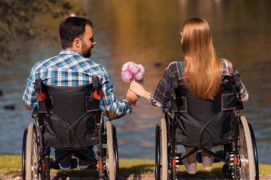 Sakatlar tekerlekli sandalye üzerinde birkaç parkta bir araya geldi. Bir erkek ve bir kadın bir buket çiçek tutuyorsun.
