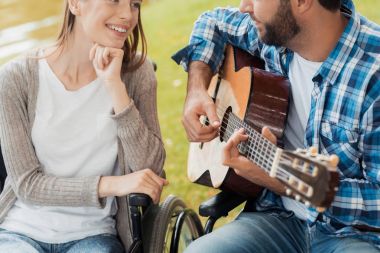 Bir erkek ve bir kadın sandalyeli parkta bir araya geldi. Bir adam gitar, kadın dinler ve gülümsüyor oynuyor.