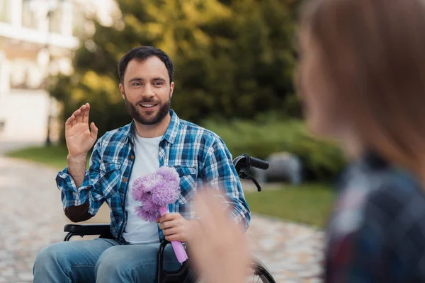 一对夫妇在轮椅上的残疾人在公园相遇。一个男人捧着一束鲜花. — 图库照片