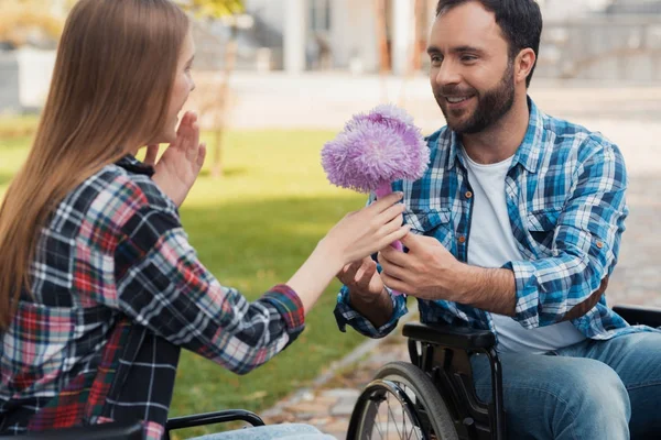 Un par de inválidos en sillas de ruedas se reunieron en el parque. Un hombre le da un ramo de flores a una mujer. . — Foto de Stock