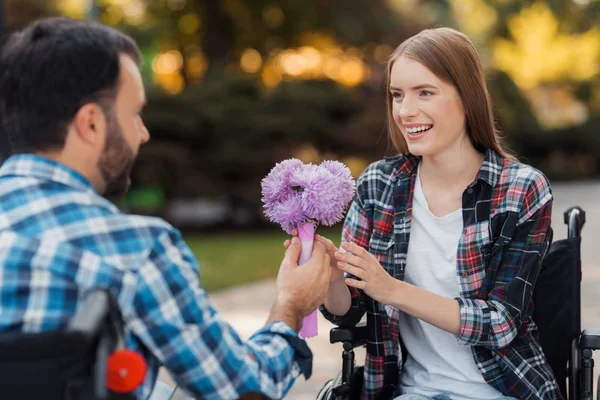 Ein paar Invaliden im Rollstuhl trafen sich im Park. ein Mann schenkt einer Frau einen Blumenstrauß. — Stockfoto