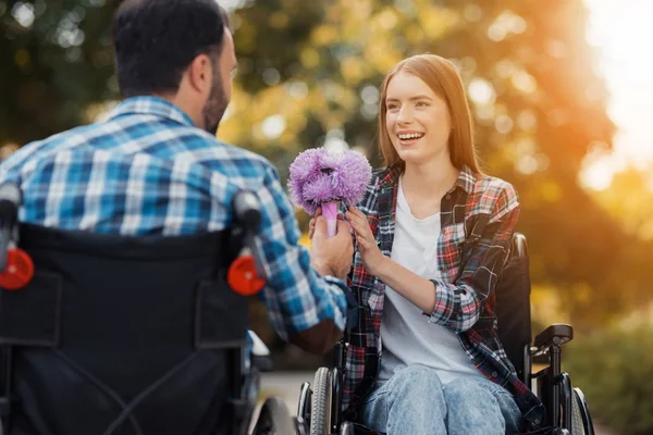 Un par de inválidos en sillas de ruedas se reunieron en el parque. Un hombre le da un ramo de flores a una mujer. . — Foto de Stock