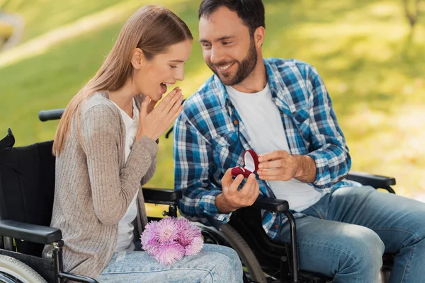 Un hombre y una mujer en silla de ruedas se conocieron en el parque. Un hombre hace de una mujer una preposesión . — Foto de Stock