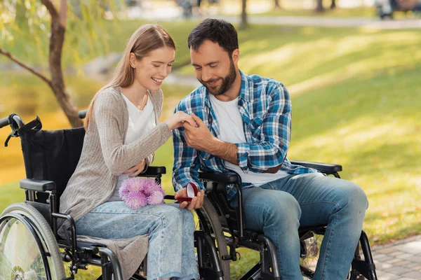 Ein Mann und eine Frau im Rollstuhl trafen sich im Park. Ein Mann legt einer Frau einen Ring an den Finger. — Stockfoto