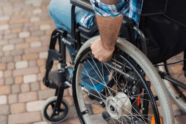 Close up. A disabled man in a wheelchair holds hands behind the wheelchair wheels. — Stock Photo, Image