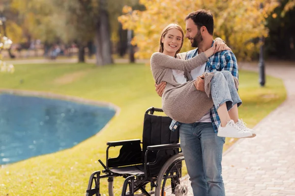 O homem está a segurar uma mulher. Atrás deles está uma cadeira de rodas. Um homem e uma mulher estão sorrindo . — Fotografia de Stock