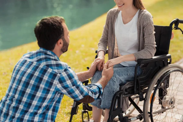 En kvinna sitter i rullstol. En man sitter bredvid henne och håller hennes händer. — Stockfoto